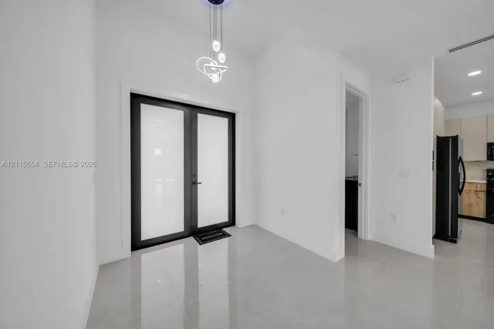 Double entry doors with matte black frames and frosted glass inserts, polished large-format tile flooring, and a modern sculptural pendant light fixture