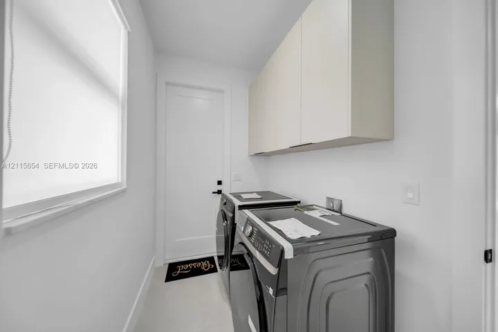 Laundry area featuring custom white cabinetry, tile flooring, a single-panel door, and a dedicated window with a roller shade