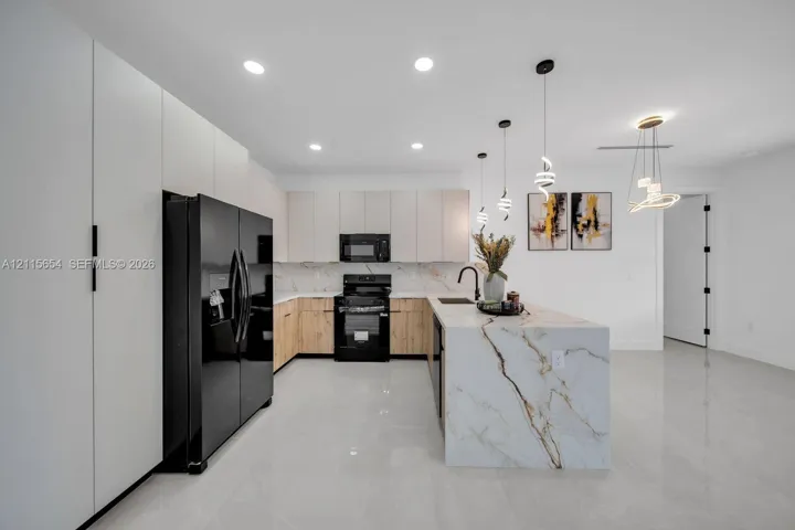Kitchen featuring white upper cabinetry, wood-finish lower cabinetry, waterfall-edge stone island, matte black hardware, and recessed lighting