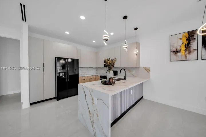 Kitchen featuring flat-panel cabinetry, a waterfall-edge island, stone-finish countertops and backsplash, recessed lighting, and three pendant fixtures