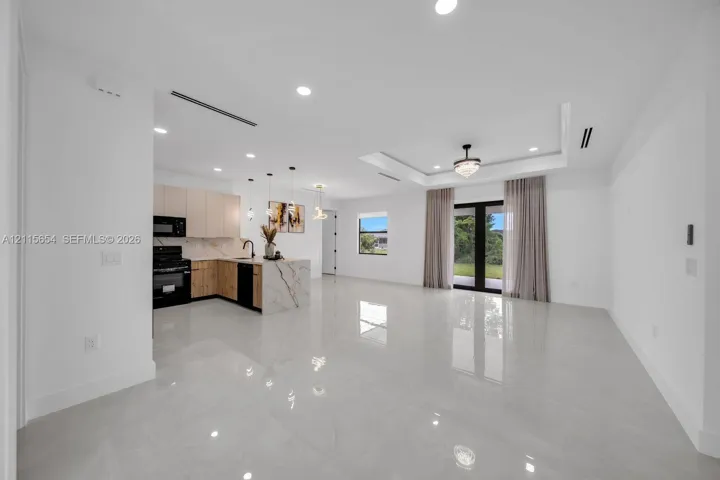 Open-concept interior featuring large-format tile flooring, tray ceilings with recessed lighting, an island with waterfall-edge stone surfacing, and dual-tone cabinetry
