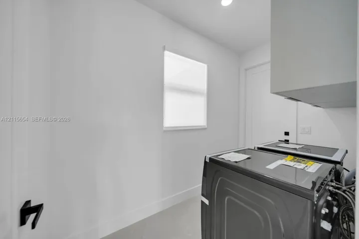 Service area featuring neutral wall finishes, a single-pane window, overhead cabinetry, and matte black door hardware