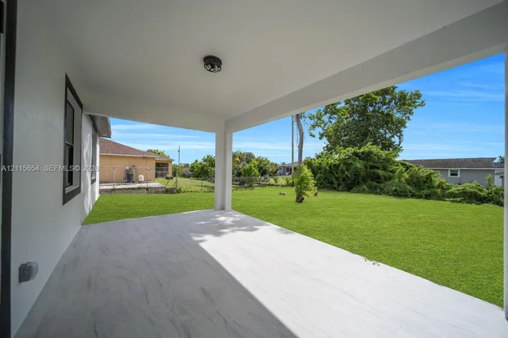 Covered patio with large-format light-toned tile flooring and an expansive, manicured lawn