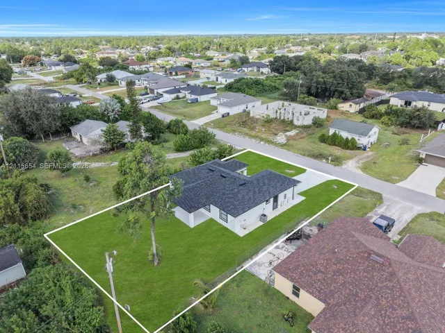 Single-story residence featuring a dark shingled roof, light-toned exterior finish, concrete driveway, and expansive grass lawn