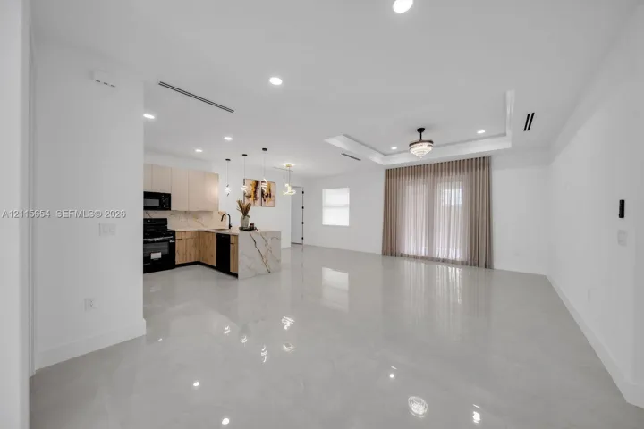 Open-concept living space featuring high-gloss tile flooring, tray ceilings with recessed lighting, and a kitchen with custom flat-panel cabinetry, stone-finish countertops, and a waterfall-edge island