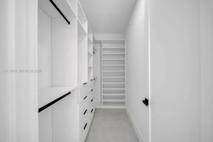 Walk-in closet featuring white built-in shelving, integrated storage drawers, hanging rods with matte black hardware, and tile flooring