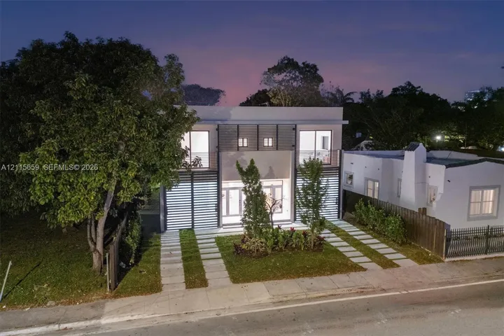 Modern two-story architectural exterior featuring smooth stucco finish, horizontal slat screening, and expansive glass entry doors