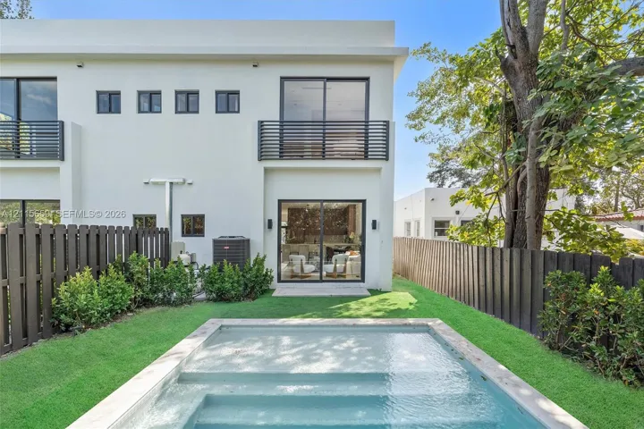 Contemporary two-story exterior featuring smooth stucco finish, black horizontal balcony railings, sliding glass doors, a rectangular swimming pool, and wood-style privacy fencing