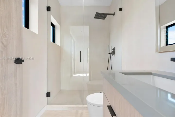 Bathroom featuring a wood-finish vanity with a stone countertop, a glass-enclosed walk-in shower with matte black rainfall showerhead, and high-contrast matte black hardware