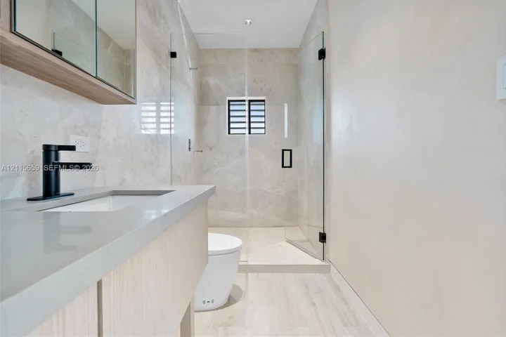 Bathroom featuring a wood-finish floating vanity, matte black faucet, full-height tile shower enclosure with a glass door, and large-format tile flooring