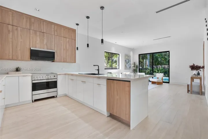 Kitchen featuring two-tone wood-finish and matte white cabinetry, stone-surfaced island, stainless steel range with overhead microwave, and wood-finish flooring