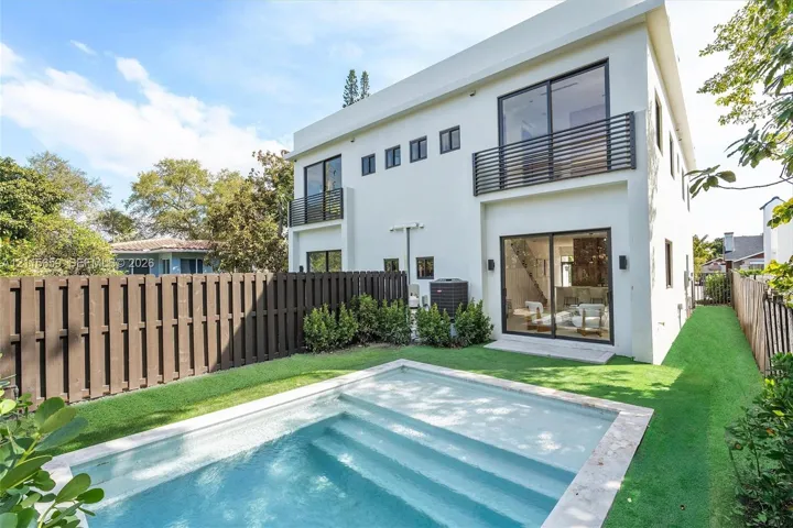 Modern two-story exterior featuring a private swimming pool with built-in steps, second-floor balconies with horizontal railings, sliding glass doors, and a wood-slat privacy fence