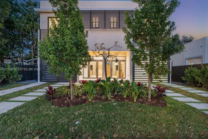 Contemporary exterior featuring clean-lined facade architecture, horizontal slat detailing, dual glass-paneled entry doors, and concrete paver pathways set within a manicured lawn