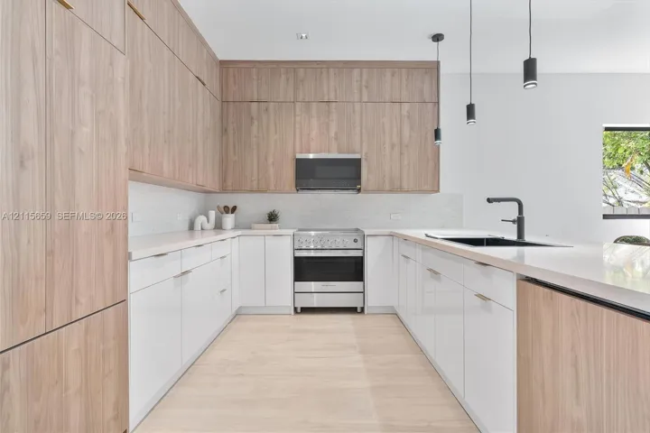 Kitchen featuring two-tone cabinetry with wood-finish upper cabinets and high-gloss lower cabinets, quartz countertops, stainless steel range with overhead microwave, and matte black plumbing fixtures