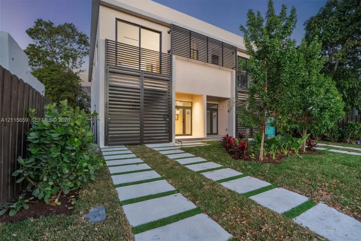 Modern two-story residence featuring a smooth stucco exterior, horizontal metal privacy screening, integrated balcony, and a permeable paver driveway system