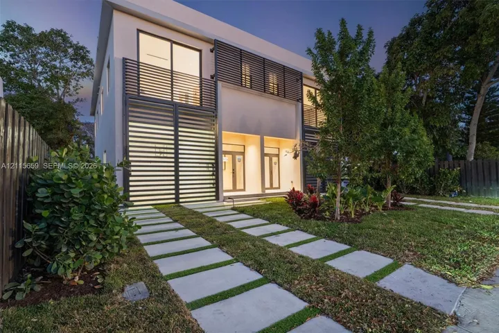 Contemporary two-story exterior featuring a smooth stucco finish, horizontal metal louvered privacy screening, glass sliding doors, and a linear paver driveway