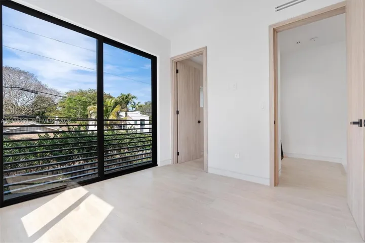 Floor-to-ceiling windows with black framing, wood-finish interior doors, light-toned wood-finish flooring, and black metal horizontal exterior railing
