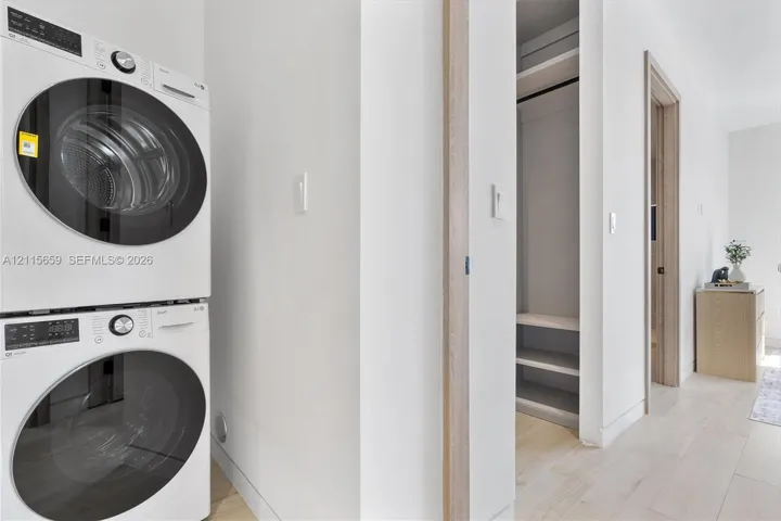 Stacked front-loading washer and dryer, built-in shelving, and light-toned wood-finish flooring