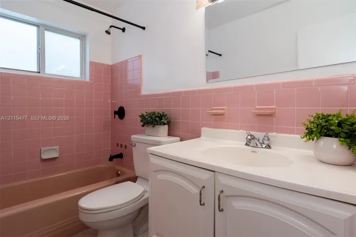 Bathroom featuring pink tile wall surround, integrated bathtub, white vanity with molded countertop, chrome dual-handle faucet, and black matte shower fixtures