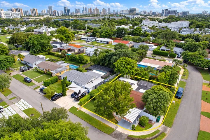 Aerial perspective featuring a corner lot property with a covered carport, mature shade trees, and perimeter fencing