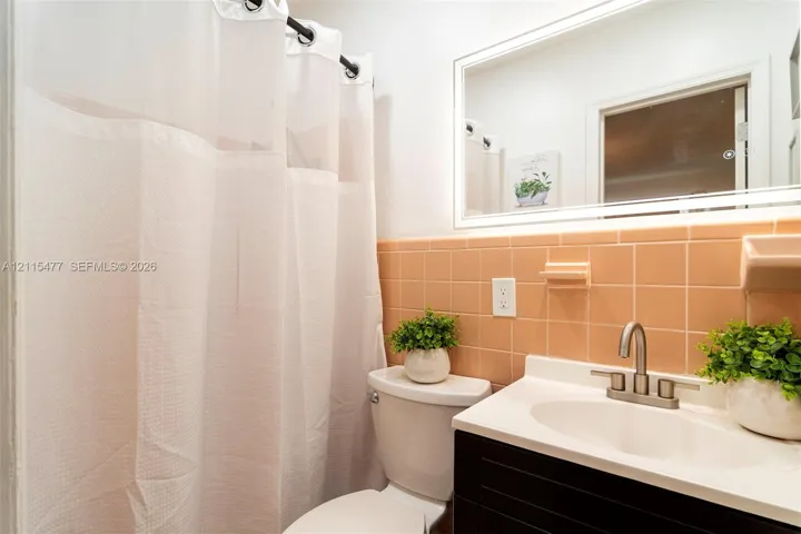 Bathroom featuring a dark-finish vanity with a white integrated sink, ceramic wall tiling, a wall-mounted mirror, and brushed-nickel faucet hardware