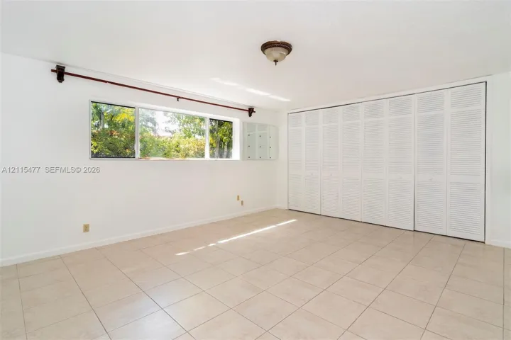 Room featuring neutral tile flooring, expansive wall-to-wall louvered-panel closets, and a large rectangular window with a window rod and finials