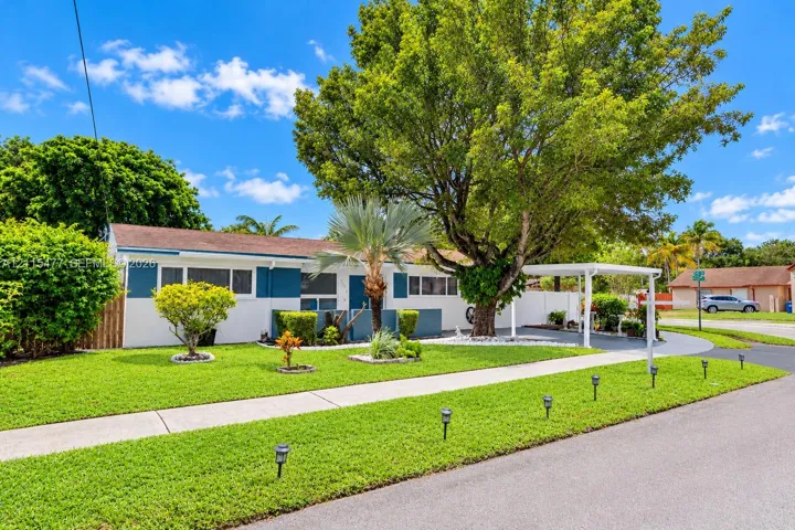 Single-story residence featuring a two-tone exterior, attached carport, manicured lawn, and mature trees