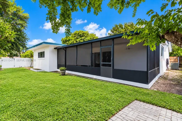 Backyard featuring a screened-in lanai, manicured lawn, paver patio, and white perimeter fencing