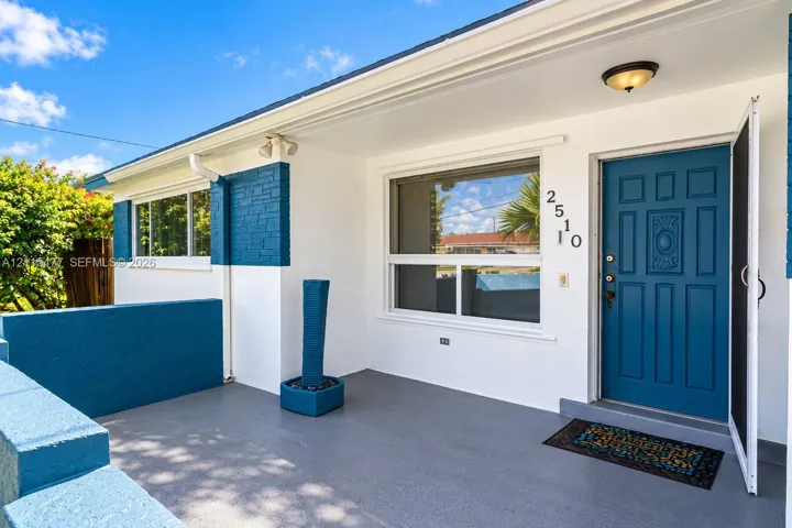 Covered entryway with concrete flooring, blue-painted masonry accents, large picture window, and paneled front door