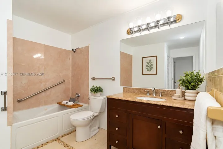 Dark wood vanity with a stone countertop, integrated sink, large wall-mounted mirror, five-light vanity fixture, and a tub with stone-tiled surround