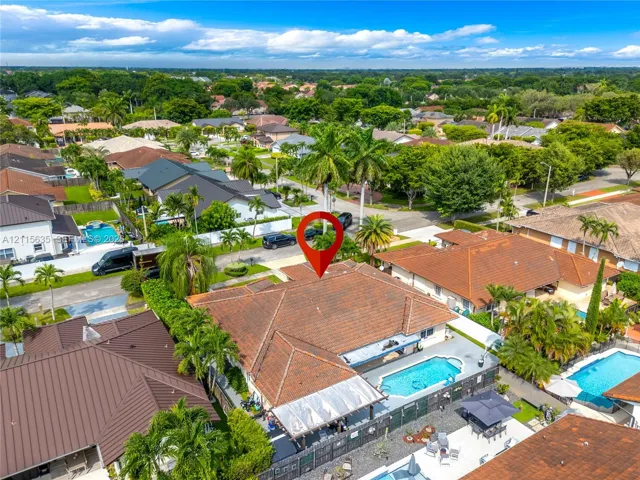 Aerial perspective of a property featuring a tile roof, an in-ground swimming pool, a paved patio area, and mature palm trees