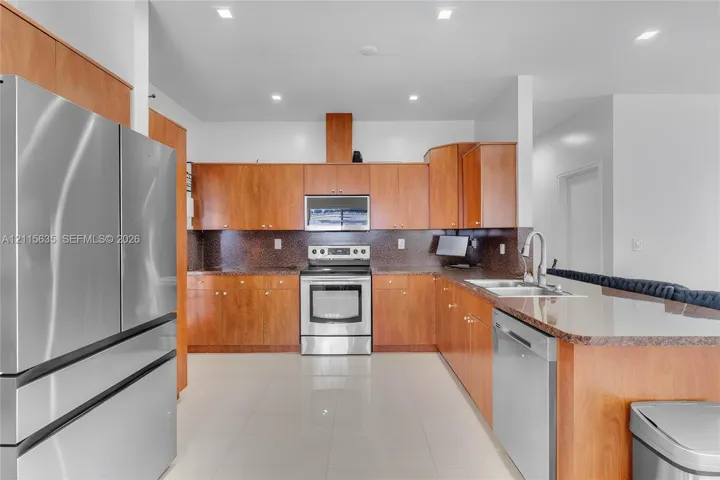 Kitchen featuring wood cabinetry, stone countertops, stainless steel appliances, a tile backsplash, and recessed lighting