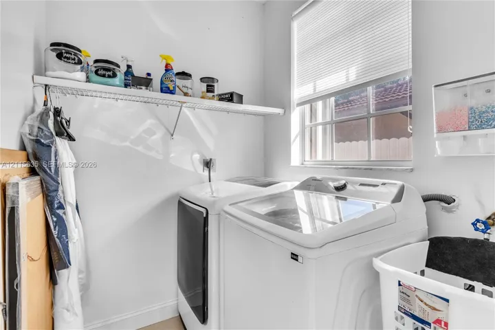 Laundry room featuring a single-hung window, white metal shelving, and a wall-mounted multi-compartment dispenser