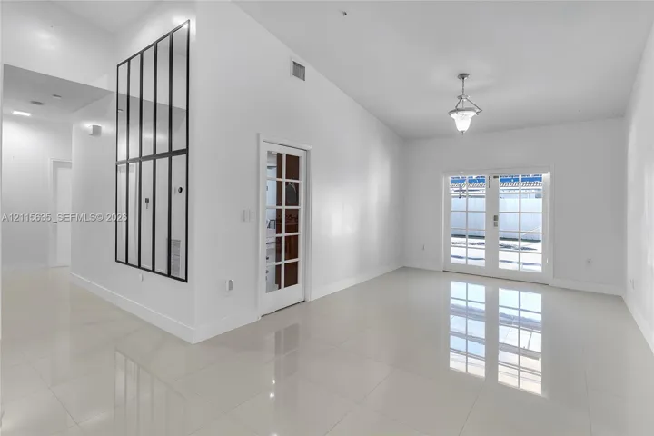 Vaulted ceiling, neutral large-format tile flooring, decorative grid-pattern wall mirror, glass-paned interior door, and double glass-paned exterior doors