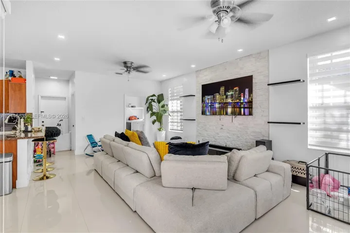 Living area featuring a floor-to-ceiling natural stone veneer accent wall, recessed lighting, ceiling fans, large-format tile flooring, and integrated wall-mounted shelving