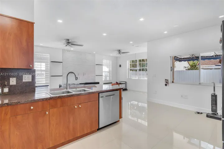 Kitchen featuring wood-finish cabinetry, stone-surface countertops, stainless steel dishwasher, recessed lighting, and tile flooring
