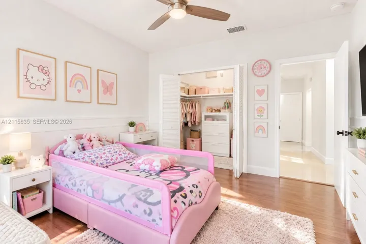 Bedroom featuring wood-finish flooring, a ceiling fan with integrated lighting, white wainscoting, and a walk-in closet with louvered double doors