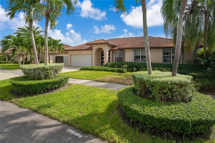 Single-story exterior featuring a concrete tile roof, stone veneer entryway, and two-car garage, surrounded by manicured landscaping and mature palm trees