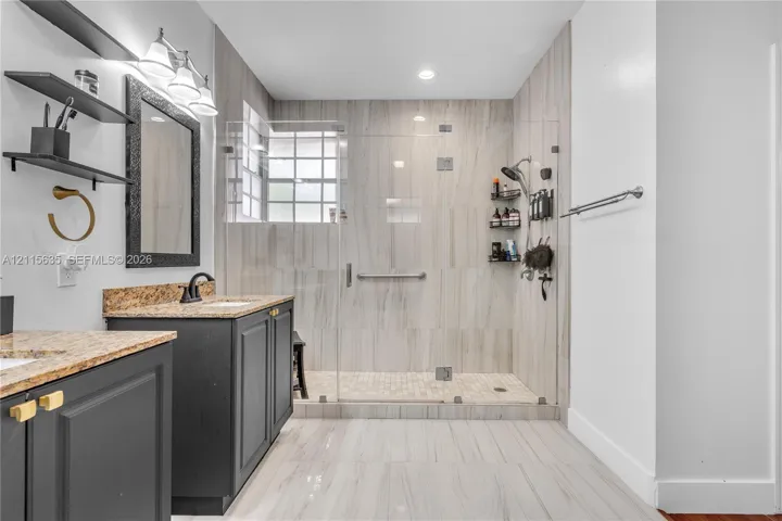 Bathroom featuring a dark wood-finish vanity with stone-surfaced countertop, walk-in shower with floor-to-ceiling tile, glass enclosure, and glass block window