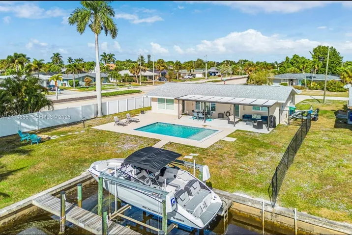 Waterfront property featuring a private boat lift, a swimming pool, a covered concrete patio, and perimeter fencing