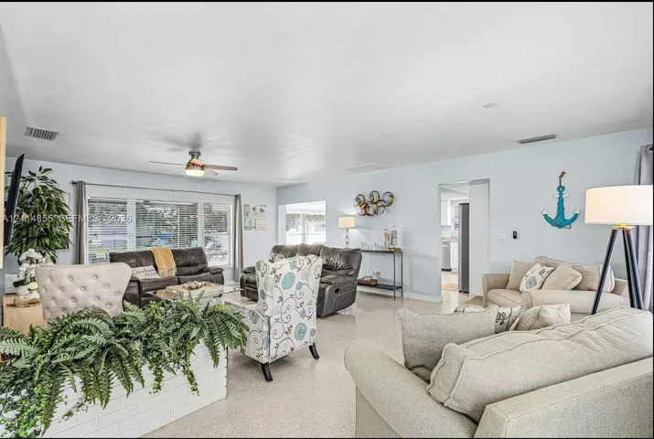 Living area featuring large windows, neutral stone-finish flooring, and a ceiling fan with integrated lighting