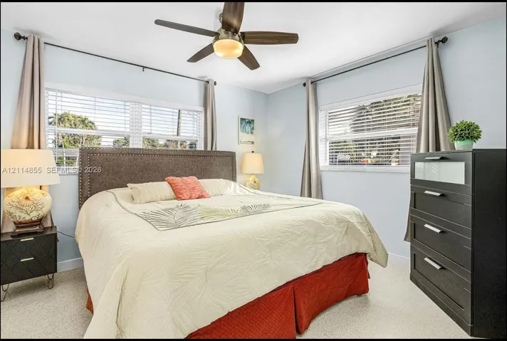 Room featuring neutral-toned carpeting, multi-pane windows with horizontal blinds, and a ceiling-mounted fan with integrated lighting