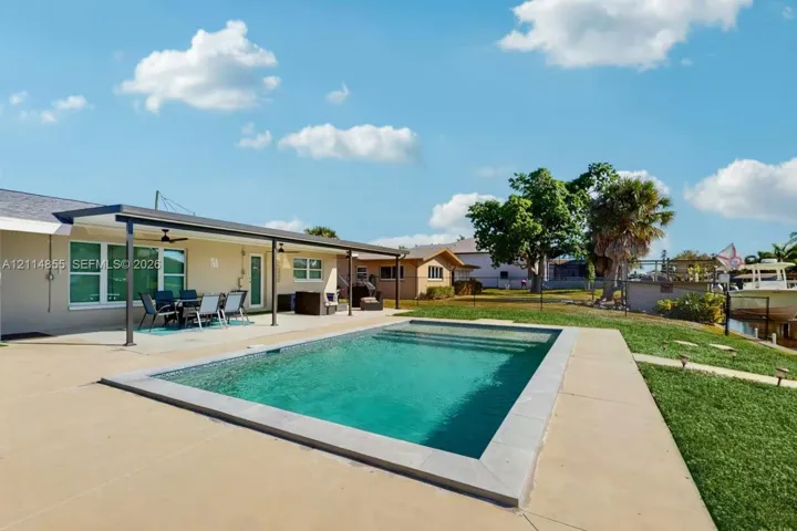 In-ground pool featuring a stone border, expansive concrete patio, and a covered lanai with ceiling fans