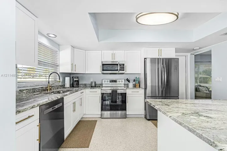 Kitchen featuring white cabinetry, stone countertops, stainless steel appliances, a high-arc faucet, and recessed ceiling lighting