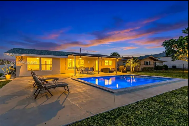 In-ground swimming pool with concrete decking, covered patio, and landscaped lawn