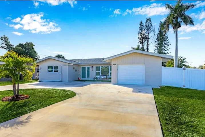 Single-story exterior featuring a concrete driveway, attached one-car garage, white vinyl fencing, and palm-accented landscaping