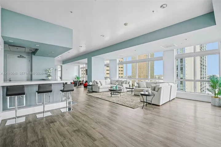Open-concept floor plan featuring expansive floor-to-ceiling windows, wood-finish flooring, recessed lighting, and a built-in wet bar with a stone-top counter