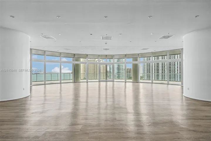 Curved interior wall architecture featuring floor-to-ceiling windows, wood-finish flooring, recessed lighting, and a wrap-around balcony