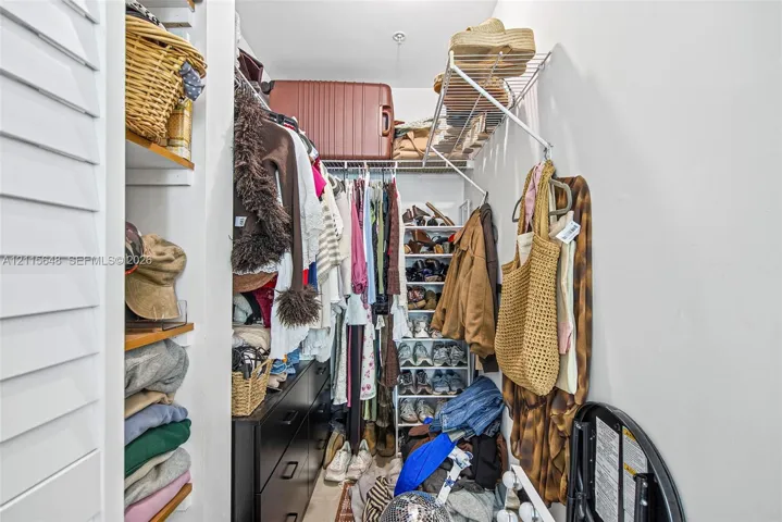 Walk-in closet featuring multi-tiered wire shelving, integrated wood-finish shelving units, and a shutter-style door