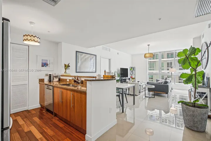 Kitchen featuring wood cabinetry, stone countertops, stainless steel dishwasher, and wood-finish flooring, complemented by floor-to-ceiling windows